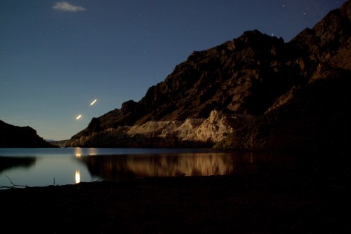 A serene night landscape featuring a calm lake reflecting mountains under a starry sky.