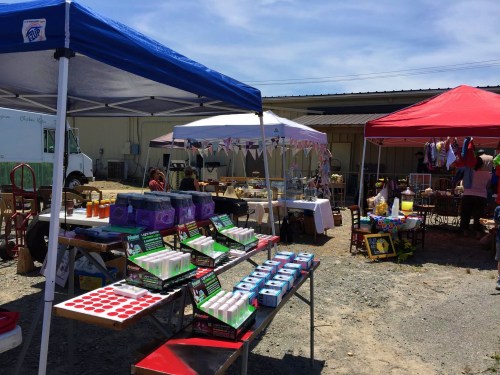 A vibrant outdoor market scene with colorful tents, tables displaying goods, and people browsing in the background.