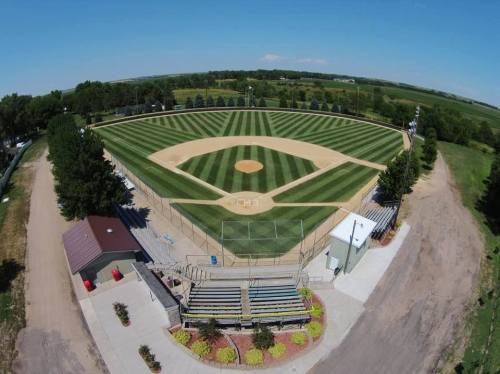 Aerial view of a well-maintained baseball field with striped grass, surrounded by trees and seating areas.