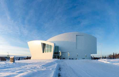 Modern white building with a unique design, surrounded by snow under a clear blue sky.