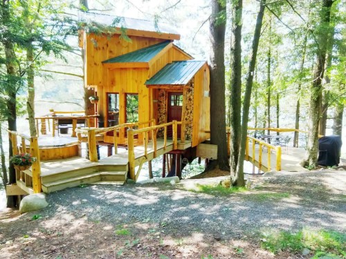 A charming wooden cabin surrounded by trees, with a deck leading to a serene lake. Sunlight filters through the foliage.