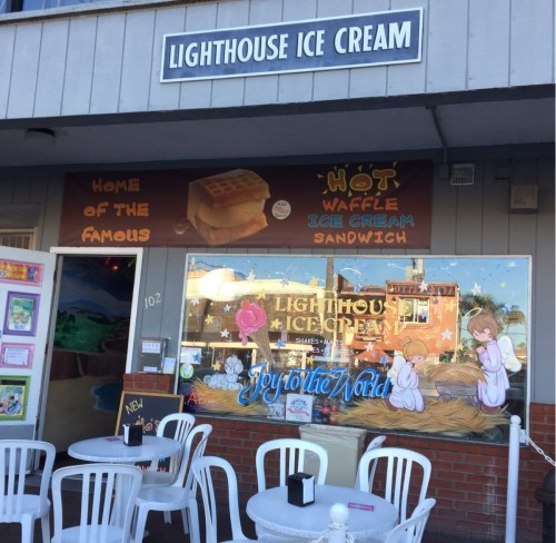 Exterior of Lighthouse Ice Cream shop with a sign, colorful window display, and outdoor seating.