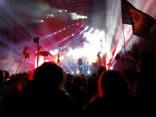 A crowd at a concert with colorful lights and flags, creating a vibrant and energetic atmosphere.