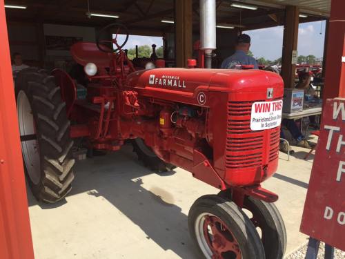 A red Farmall tractor displayed in a barn, with a sign promoting a raffle to win it.