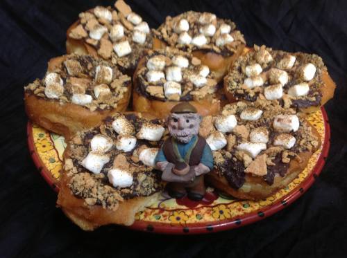A plate of chocolate-covered pastries topped with marshmallows and graham cracker crumbs, with a small figurine in the center.