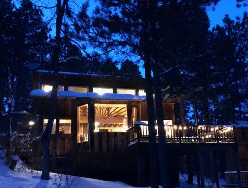 A cozy wooden cabin illuminated at night, surrounded by snow-covered trees.