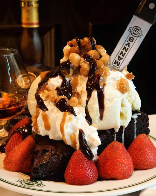 A decadent dessert featuring a brownie topped with ice cream, whipped cream, chocolate sauce, nuts, and fresh strawberries.