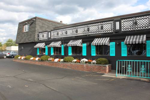 A black building with turquoise windows and striped awnings, featuring a flower bed along the front and a parking area.