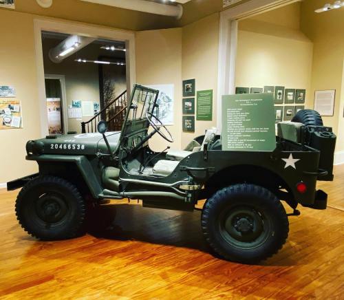 A vintage military jeep displayed in a museum, featuring a green exterior and a star insignia.