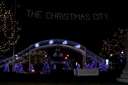 A festive display of lights and decorated trees under a sign reading "THE CHRISTMAS CITY" at night.