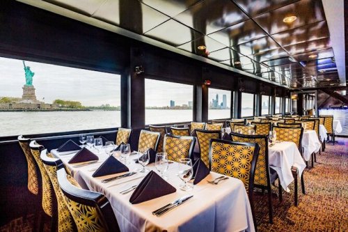 Elegant dining area with tables set for a meal, featuring a view of the Statue of Liberty through large windows.