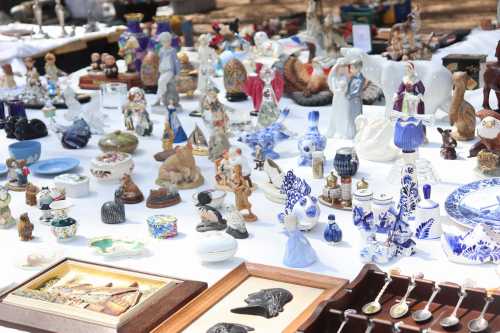 A variety of colorful antiques and collectibles displayed on a table at a market, including figurines and decorative items.