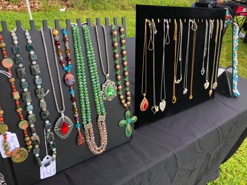 Display of colorful necklaces and pendants on black stands at an outdoor market.