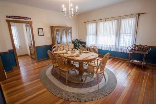A cozy dining room with a wooden table, chairs, and a china cabinet, featuring warm wood floors and blue walls.