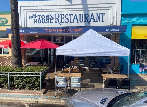 Exterior of Old Town House Restaurant with outdoor seating, umbrellas, and a tent in front. Bright, sunny day.