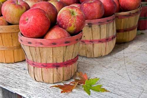 Baskets of red apples on a wooden table, with a colorful autumn leaf nearby.