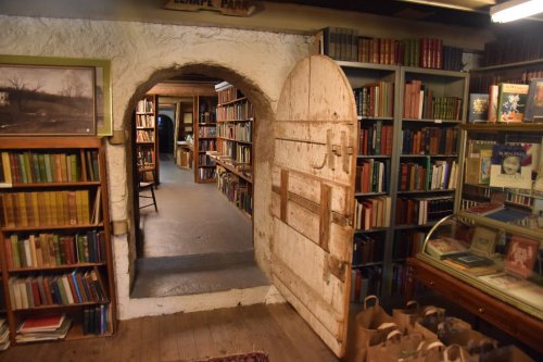 A cozy library with wooden shelves filled with books, featuring an arched doorway and a vintage wooden door.