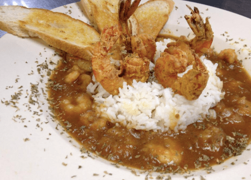 A plate of shrimp over white rice, garnished with herbs, accompanied by toasted bread slices.