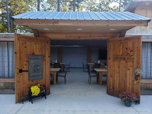 A rustic wooden entrance with open doors leading to a cozy dining area, decorated with flowers and warm lighting.