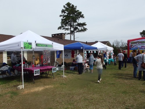 A community event with tents selling various items, people browsing, and a grassy area under a cloudy sky.