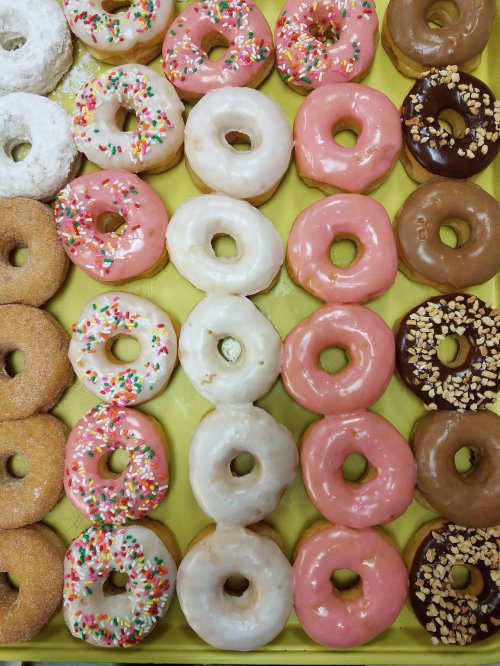 A colorful assortment of donuts, including glazed, frosted, and sprinkled varieties, arranged in a tray.