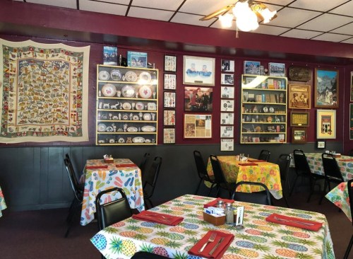Cozy restaurant interior with colorful tablecloths, decorated walls featuring plates, photos, and a quilt.