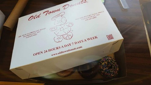A white donut box from Old Town Donuts with colorful donuts peeking out, placed on a wooden table.