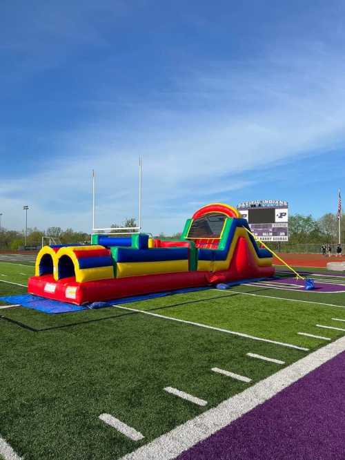 A colorful inflatable bounce house on a sports field under a clear blue sky.