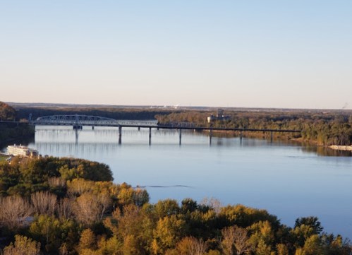 A serene river scene with a bridge, surrounded by autumn foliage and clear blue skies.
