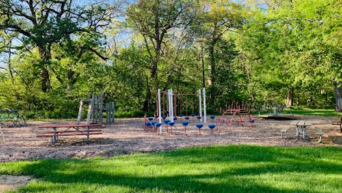 A playground with colorful equipment surrounded by trees and grassy areas on a sunny day.