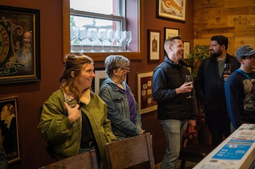 A group of people enjoying a wine tasting in a cozy, decorated room, holding glasses and smiling.