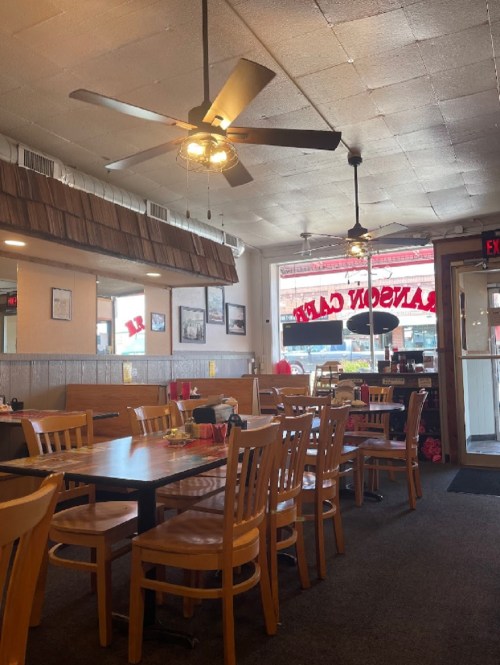 Cozy diner interior with wooden tables, chairs, and a ceiling fan, featuring a welcoming entrance and bright windows.