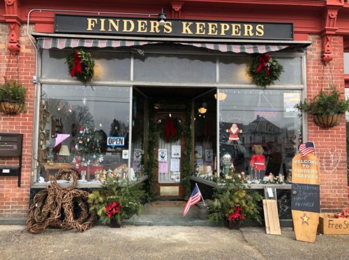 A festive storefront with holiday decorations, including wreaths and lights, and a sign reading "Finders Keepers."