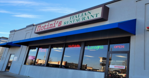 Exterior of Notini's Italian Restaurant, featuring a blue awning and large windows with colorful signs for menu items and "OPEN."