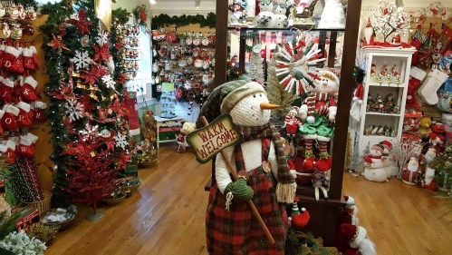 A festive shop filled with holiday decorations, featuring a snowman holding a "Happy Welcome" sign amidst Christmas decor.