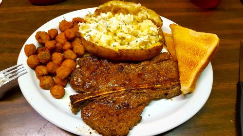 A plate with a grilled steak, baked potato with toppings, fried okra, and a slice of toast.