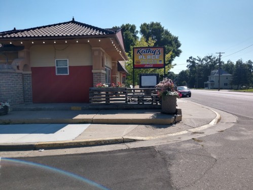 A corner view of Kathy's Place restaurant with outdoor seating and a colorful sign on a sunny day.