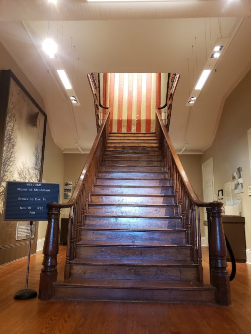 A wooden staircase leads to a brightly lit upper level, adorned with an American flag mural.
