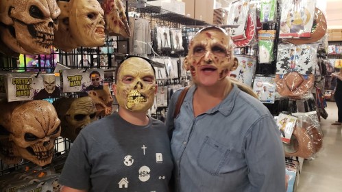 Two people wearing creepy skull masks stand in a store filled with Halloween costumes and accessories.