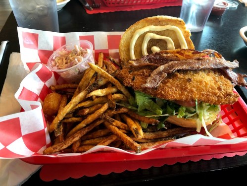 A basket of food featuring a fried chicken sandwich, fries, coleslaw, and a waffle on a red checkered tray.