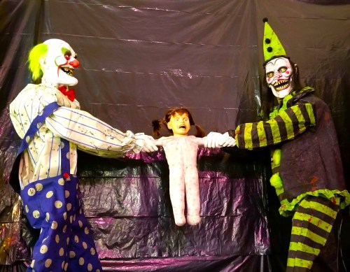Two creepy clowns pull a terrified doll in a dark, eerie setting.