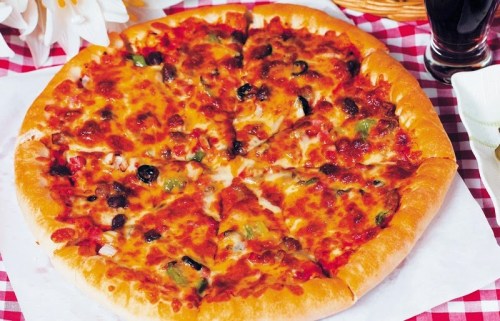 A freshly baked pizza topped with cheese, olives, and vegetables, served on a checkered tablecloth.