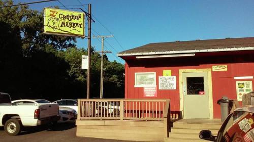 A red building with a sign reading "Cysure Market," featuring a porch and parked cars nearby.
