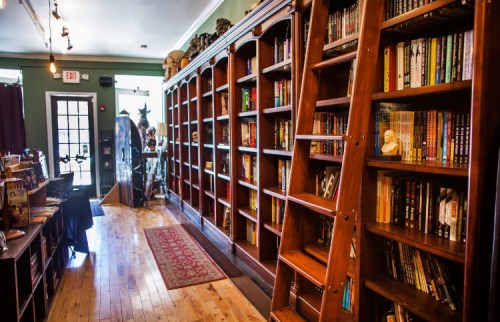 A cozy bookstore interior featuring wooden shelves filled with books and a ladder for access. Warm lighting enhances the atmosphere.