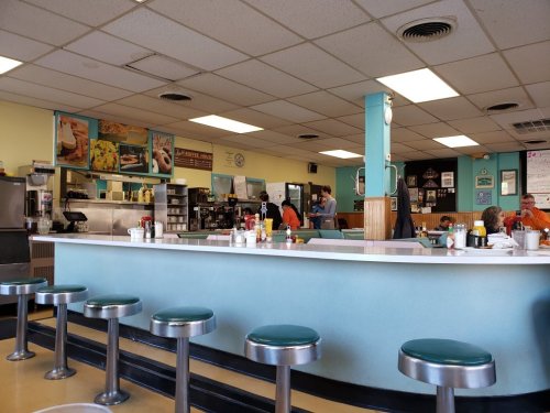 A retro diner interior with a counter, stools, and staff serving customers in a casual setting.