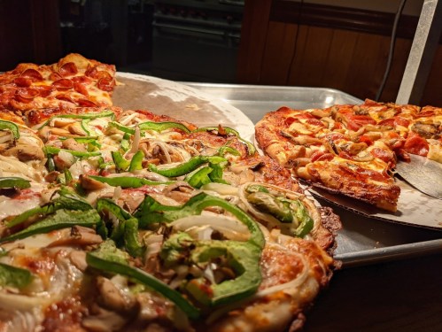 A tray of three pizzas: one with pepperoni, one with green peppers and chicken, and another with mixed toppings.