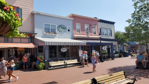 A sunny street scene with colorful storefronts and people walking, enjoying a vibrant outdoor atmosphere.