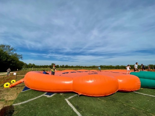 A large orange inflatable structure in a field, with children playing and a clear blue sky above.
