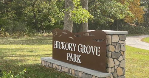 Sign for Hickory Grove Park, featuring stone base and surrounded by trees and greenery.