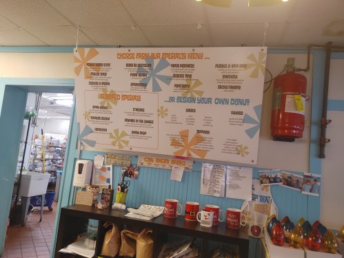 Menu board featuring specialty donuts and options to design your own, with colorful graphics and a fire extinguisher nearby.